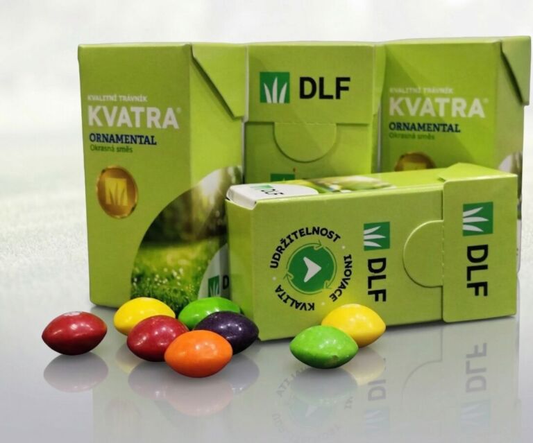 Dárková krabička s barevným logem DLF a motivem zeleného trávníku, vedle které jsou vysypané barevné bonbony Skittles na čistém bílém pozadí.